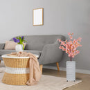 Sofá cinza moderno com mesa de vime, flores artificiais e vaso branco em decoração de sala
